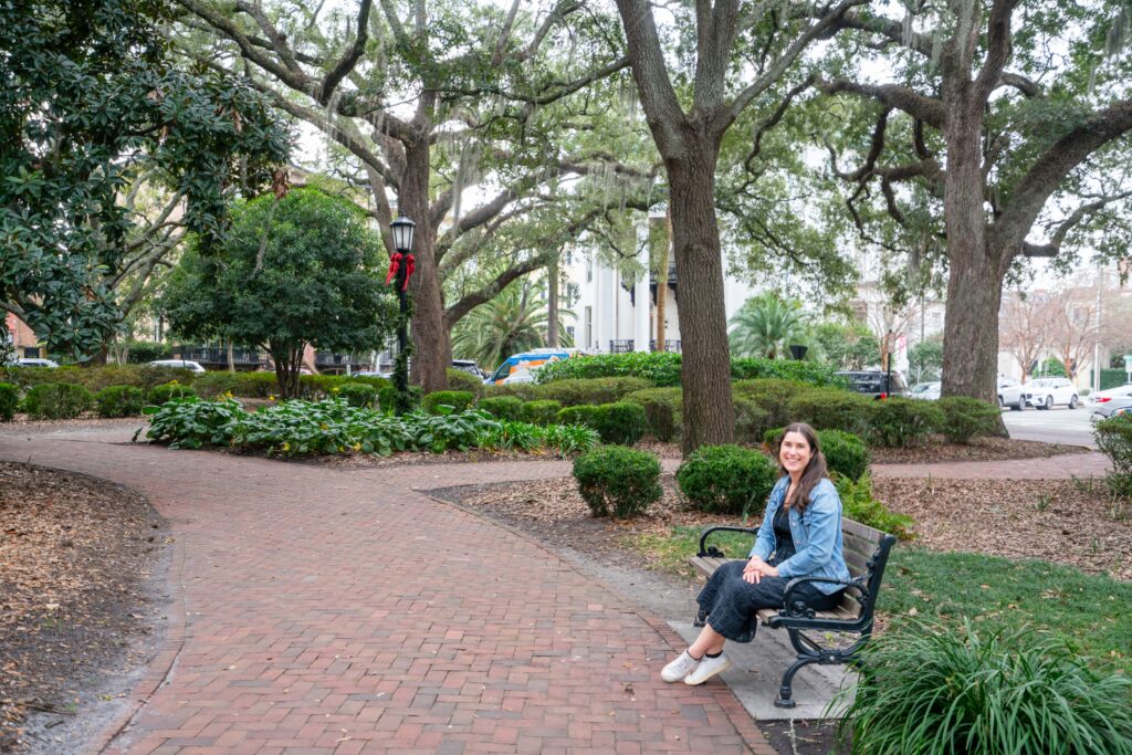 kate storm sitting on a bench in chippewa square savannah january with christmas decor on a light post behind her