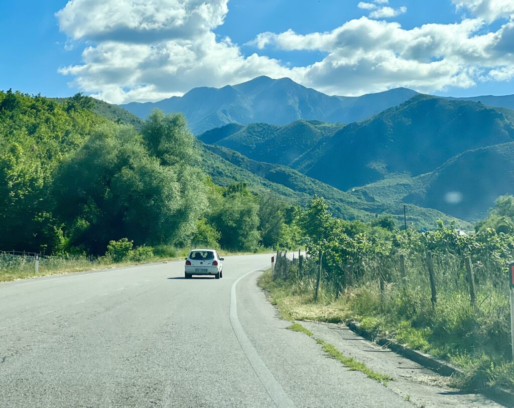 rural road in albania with white car in the distance and mountains beyond, taken through a windshield