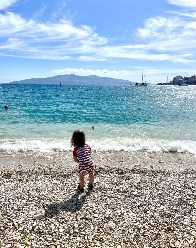 young toddler throwing a pebble into the water at saranda's public beach, visiting the beach is one of the best things to do in saranda albania