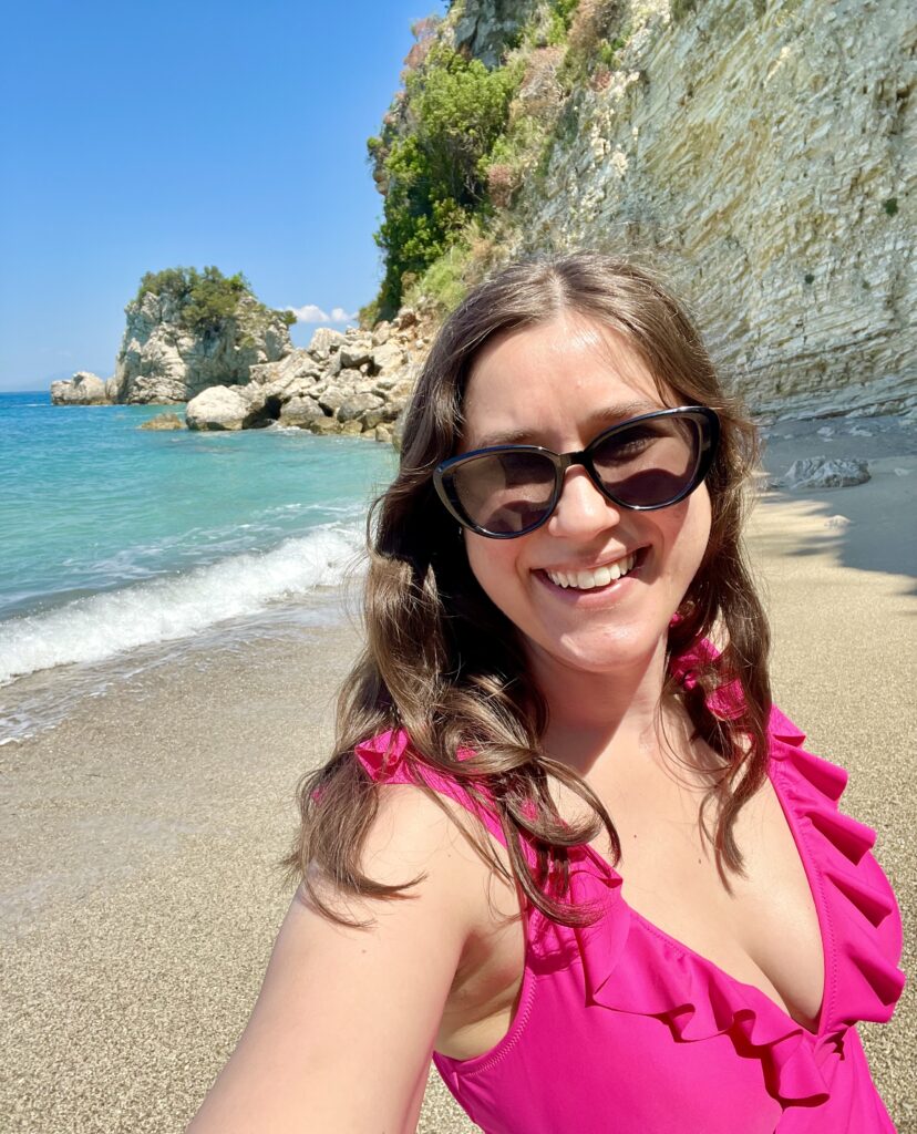 kate storm in a pink bathing suit and sunglasses taking a selfie on mirror beach albania