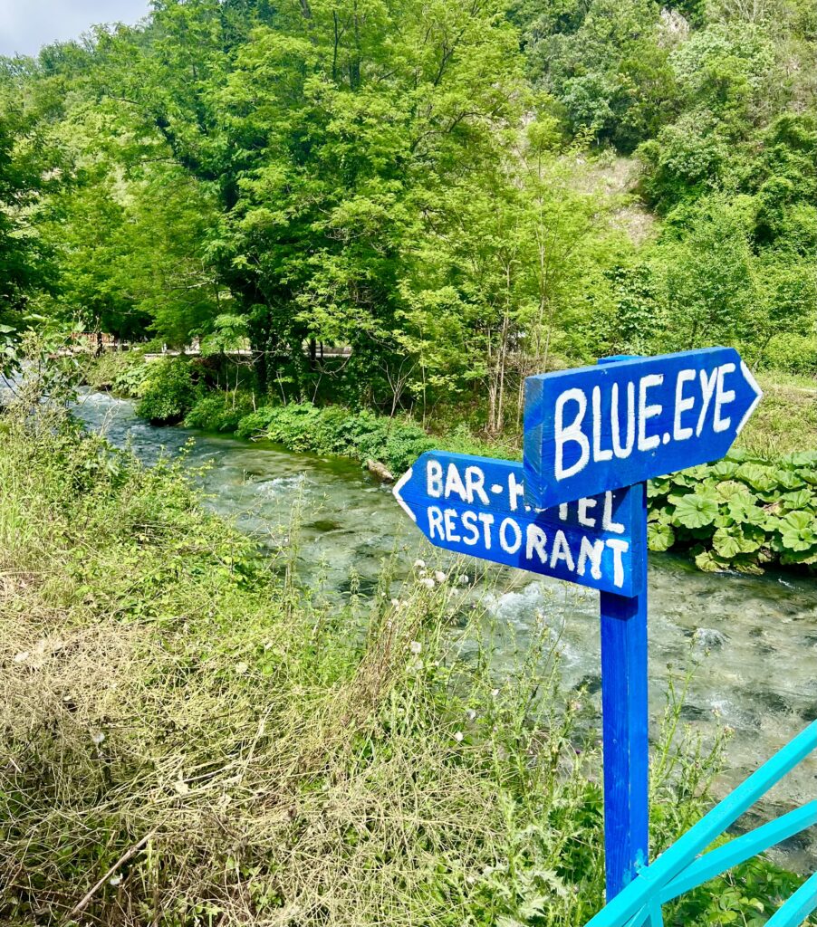 view of a sign for the blue eye near a bridge crossing, surrounded by foliage