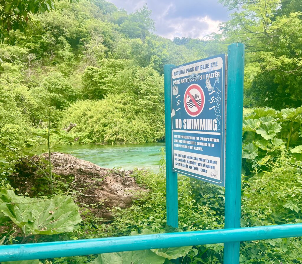 large sign at the saranda blue eye albania stating that no swimming is allowed