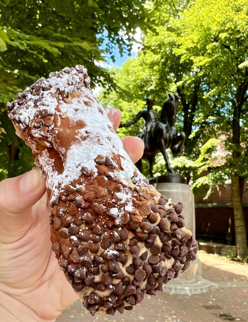 espresso cannoli from mikes pastry being held up in front of paul revere statue when visiting the north end boston ma
