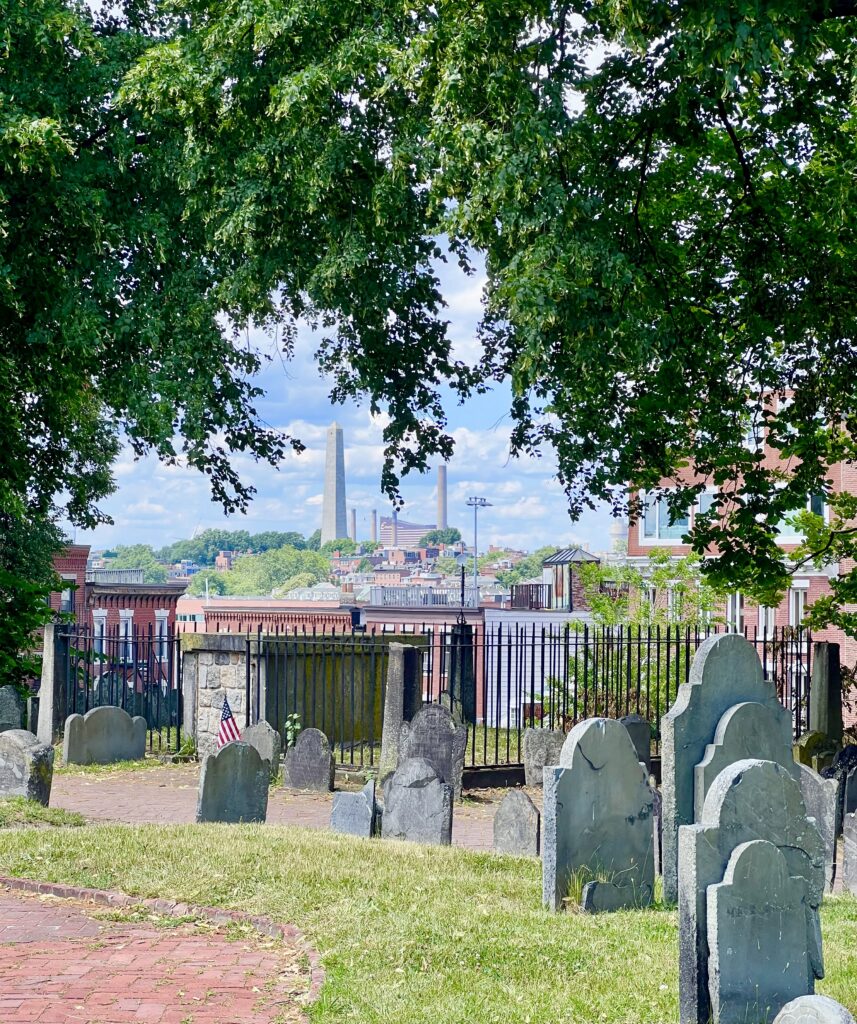 bunker hill monument and charlestown as seen from copp's hill burying ground on boston freedom trail, with stones and trees in the foreground