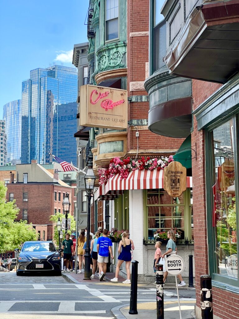view of a street in the north end boston's little italy with italian restaurant to the right and modern buildings visible in the distance