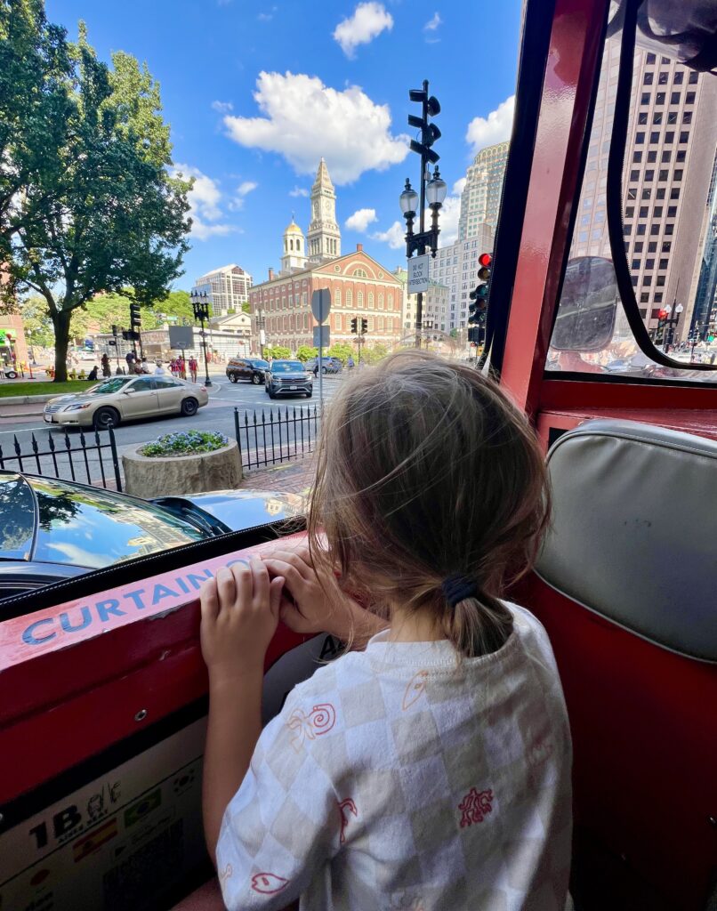 young toddler looking out the window of a boston duck boat with city buildings in the background