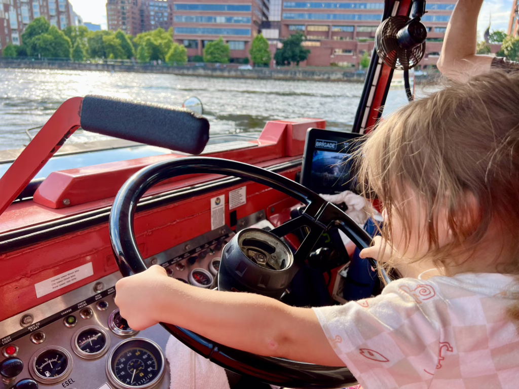 young toddler holding the steering wheel of a boston duck boat during a duck tour in boston ma