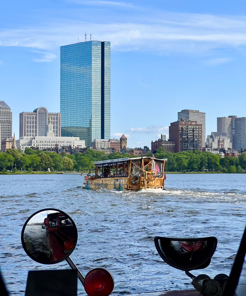 boston duck boat on the charles river with skyscraper in the background, as seen from another duck boat