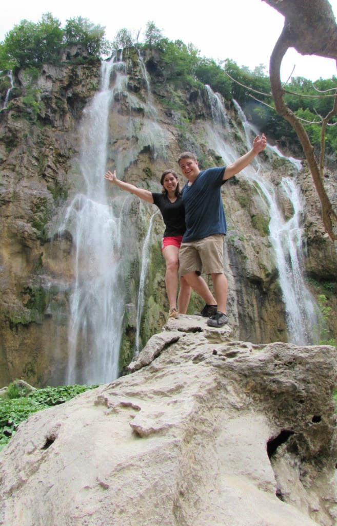 Kate Storm and Jeremy Storm standing on a boulder in front to Veliki Slap with their arms out