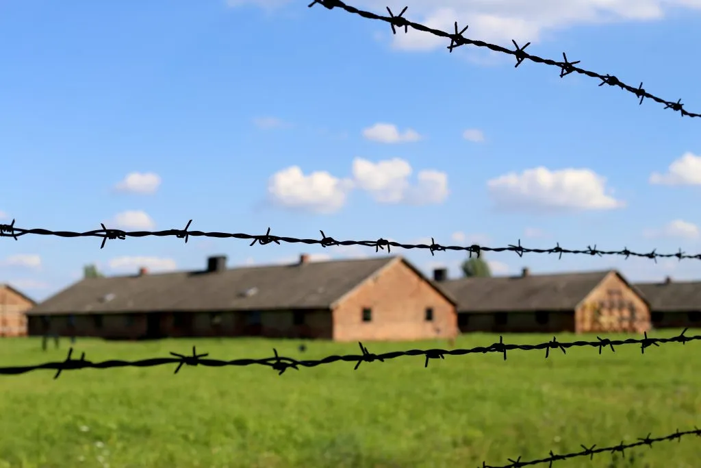 barracks of birkenau concentration camp as seen through barbed wire fence