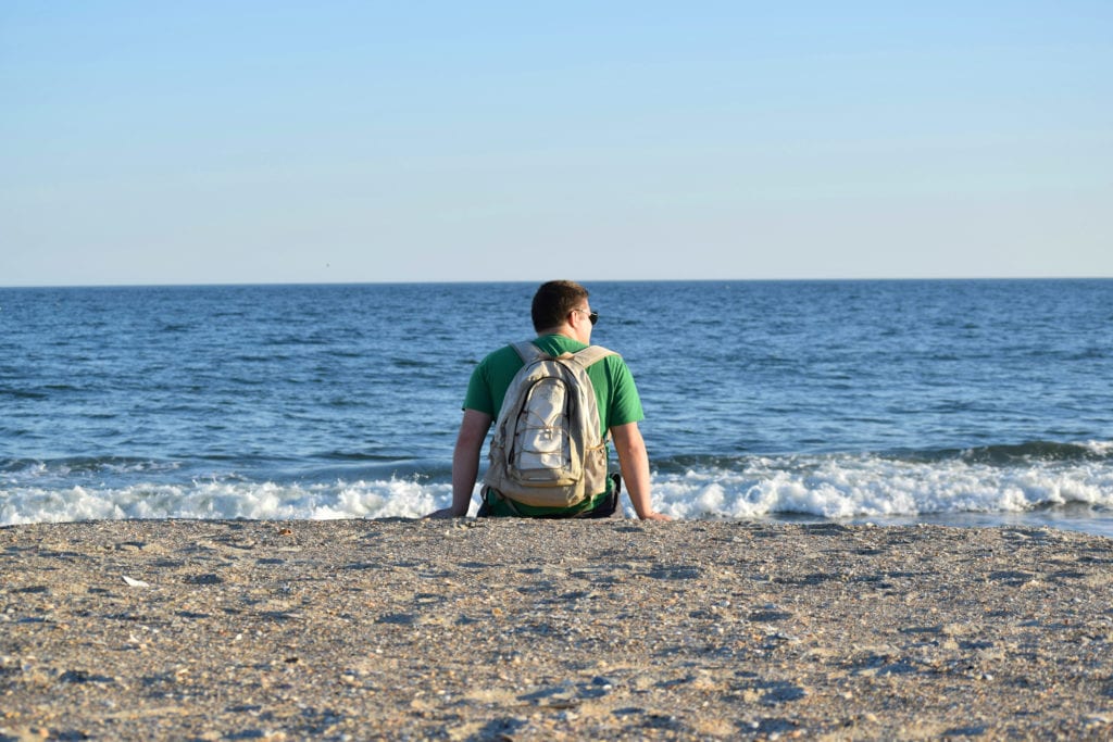 Jeremy Storm sitting on the beach at Fort Macon State Park North Carolina wearing a backpack and overlooking the ocean