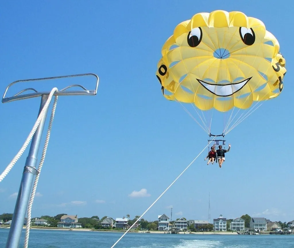 Kate Storm and Jeremy Storm seated below a bright yellow parasail that is over the Bogue Sound. Parasailing is one of the fun things to do in Atlantic Beach NC