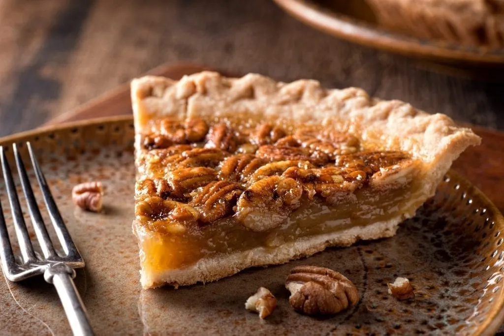 Slice of pecan pie with a fork on the left side fo the photo