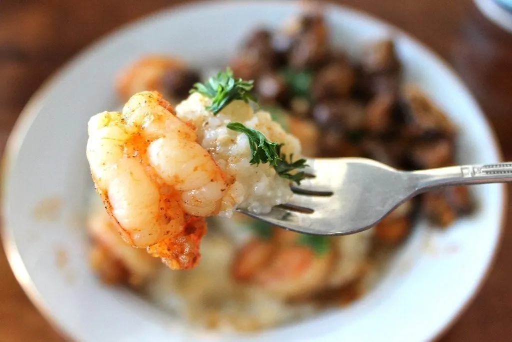 Plate of shrimp and grits with a bite on a fork being held in the foreground