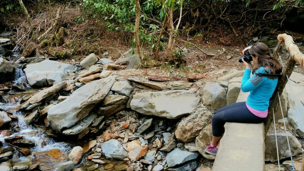 kate storm snapping a photo while hiking in great smoky mountains national park while sitting on a footbridge
