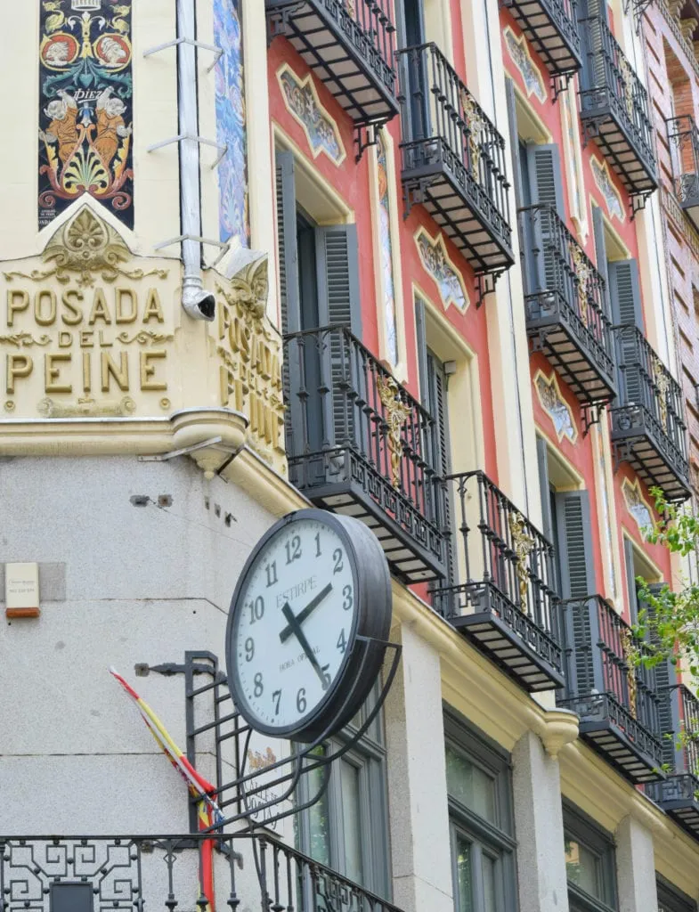 Clock attached to a red building with black wrought iron balconies in Madrid Spain--you'll see plenty of beautiful buildings like this during your 3 days in Madrid!