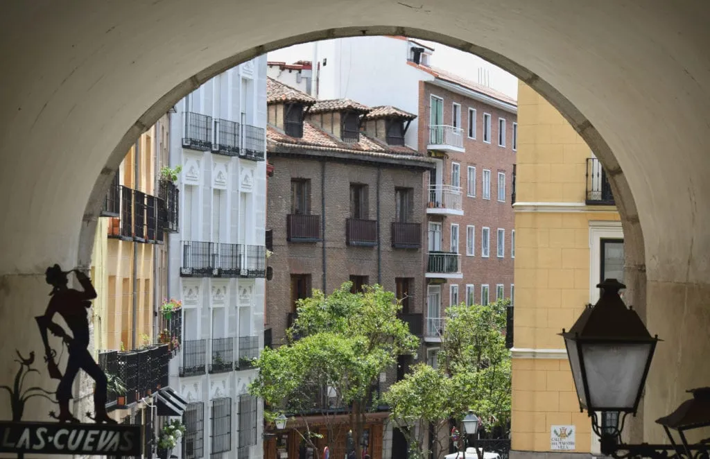 Photo of an arch in Madrid Spain with colorful buildings visible in the background
