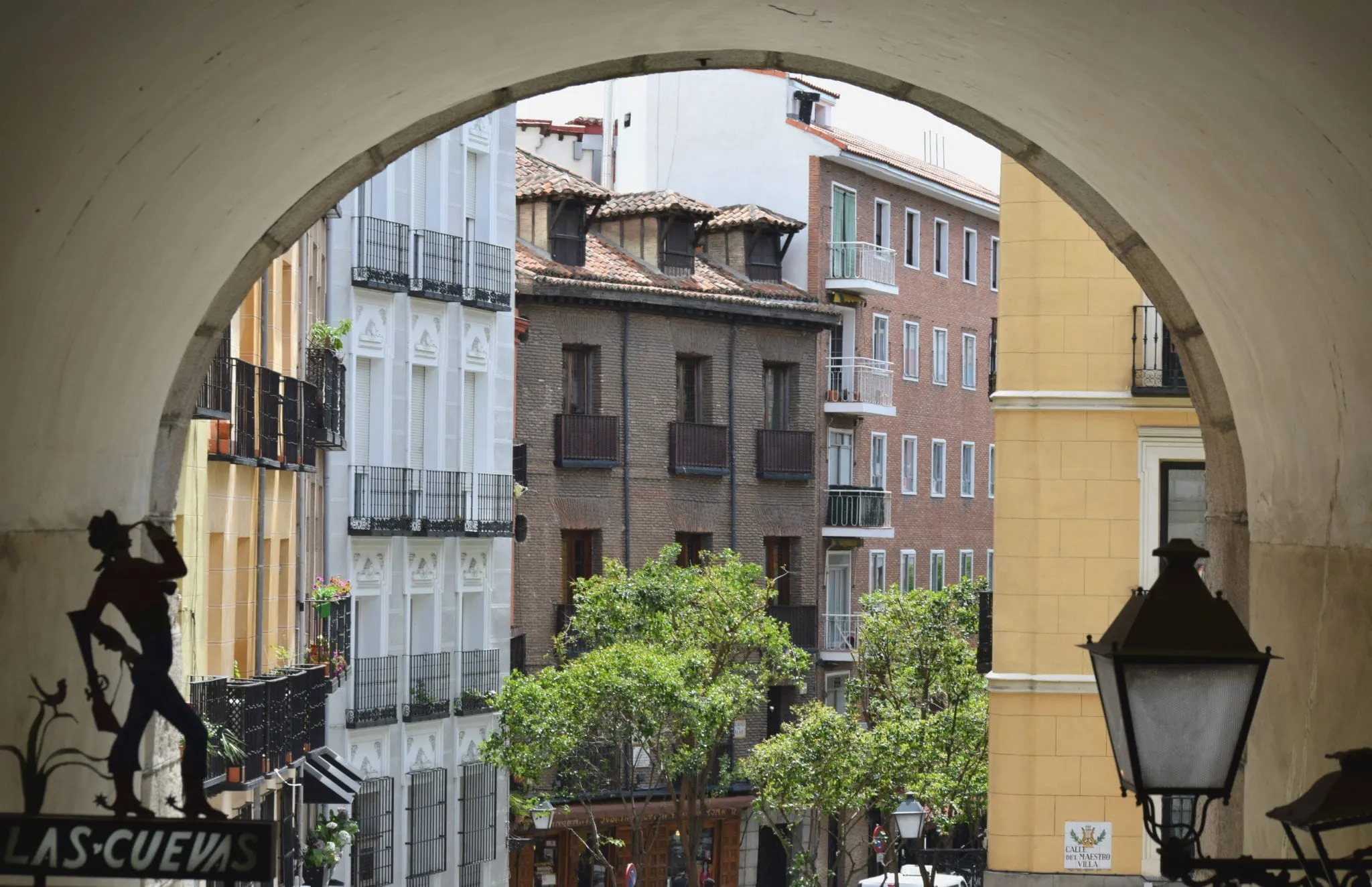 Photo of an arch in Madrid Spain with colorful buildings visible in the background. views like this are a free way to enjoy madrid on a budget