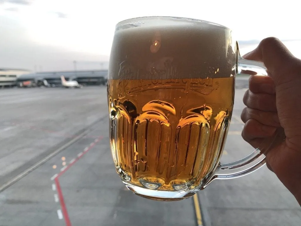 Czech Beer in Prague Airport being held against a window with planes in the background--beer definitely isn't a long haul flight essential, but it is tasty