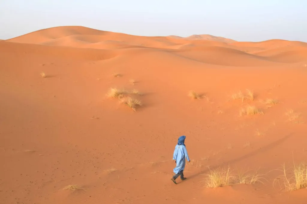 young boy in blue walking across a sand dune during morocco desert tours