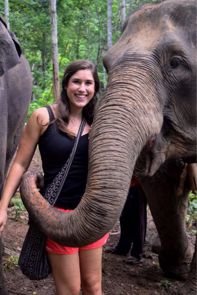 kate storm posing with an elephant in thailand that has its trunk wrapped around her waist