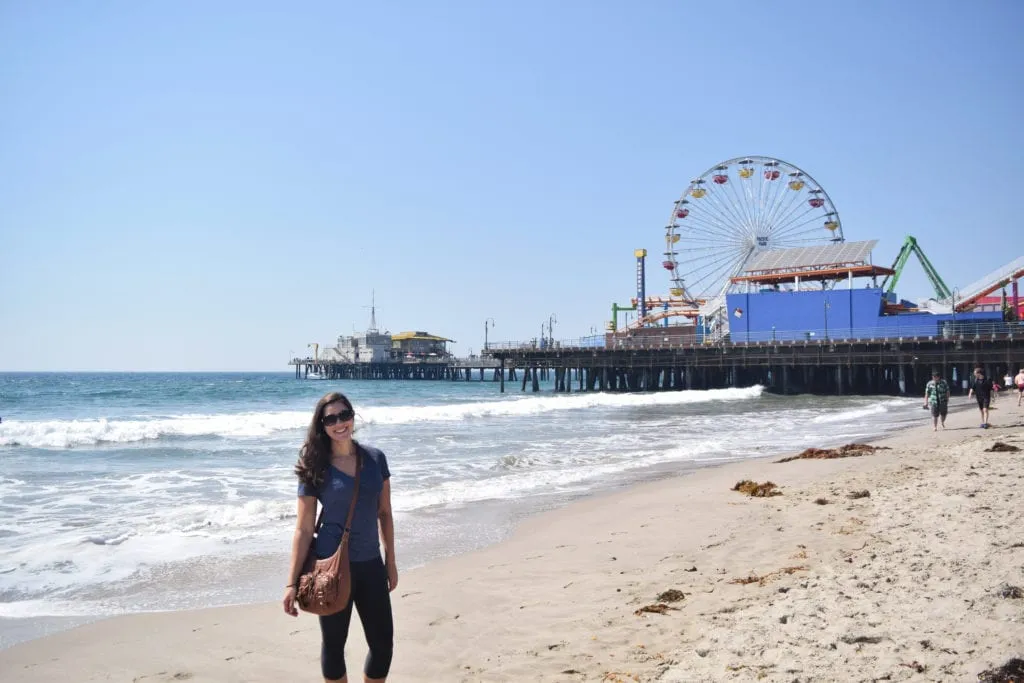 Kate Storm standing on the beach next to Santa Monica Pier is Los Angeles, California, the final destination of some of the most classic USA road trip itinerary ideas