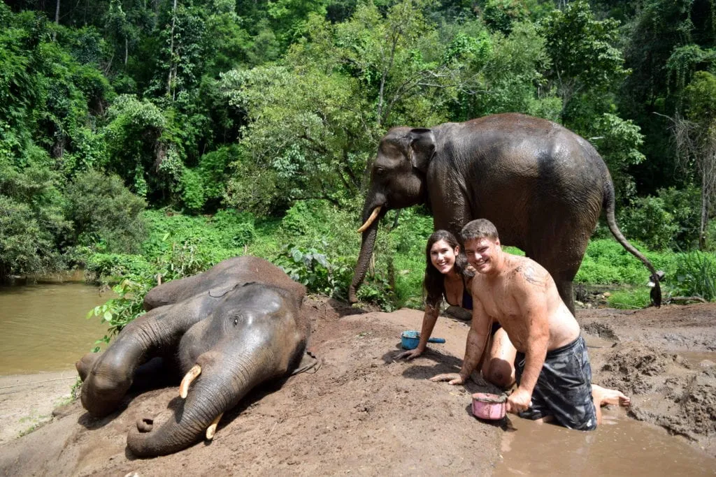 kate Storm und Jeremy Storm mit zwei Elefanten, die sie in Thailand baden, wenn sie die Welt mit dem Rucksack bereisen