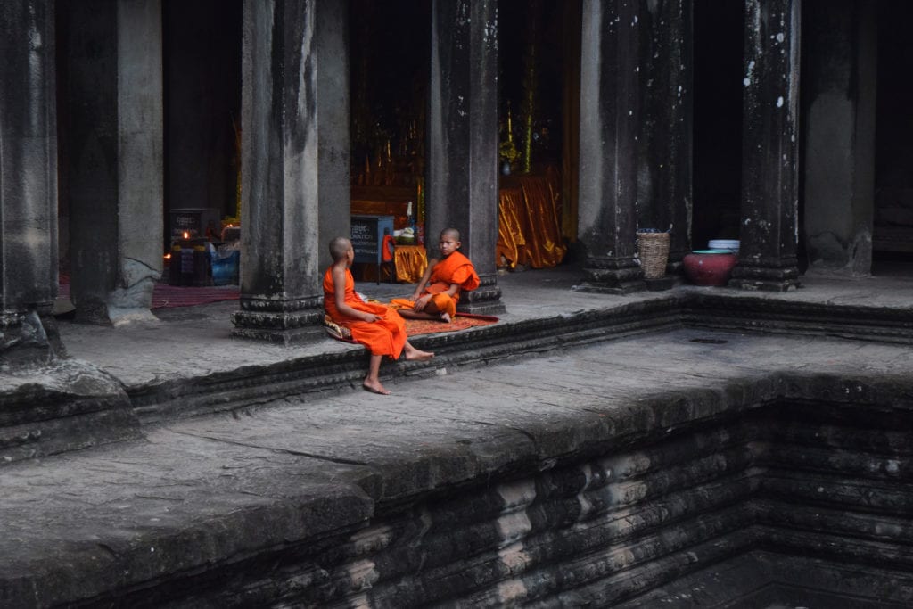 two young monks in orange robes sitting on a temple structure in angkor wat siem reap