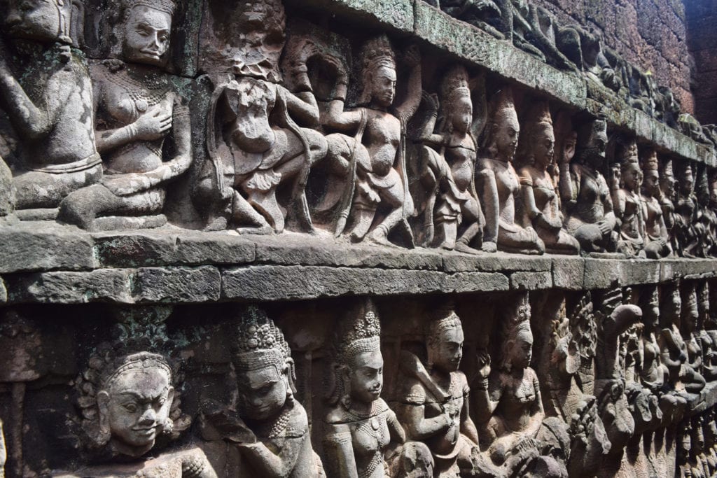 detailed carvings of human figures in a wall in cambodia