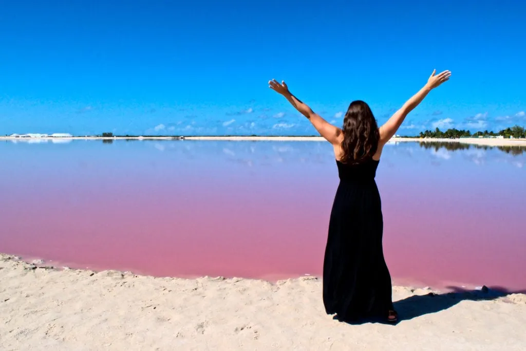 Kate Storm in a black maxi dress standing in front of one of the pink lakes las coloradas mexico