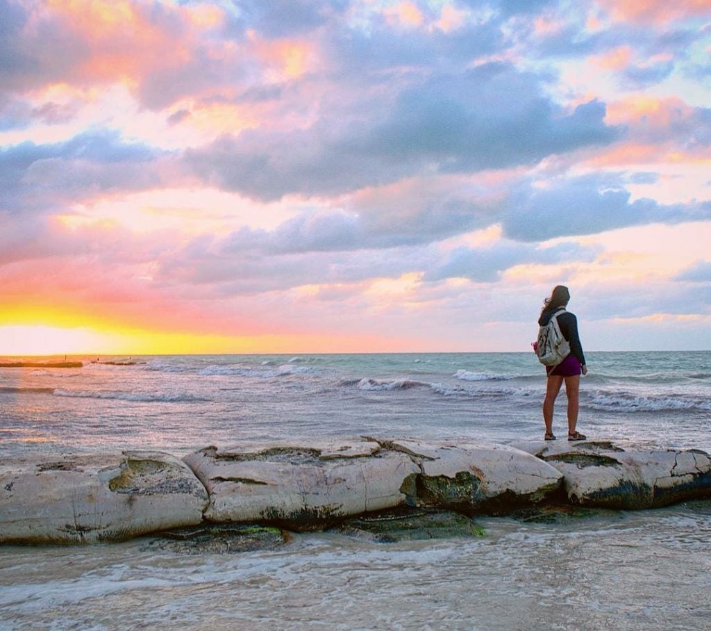 kate storm standing on the beach looking at a sunset on holbox island mexico