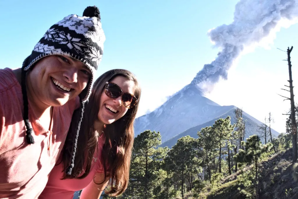kate storm and jeremy storm in front of volcan de acatenango as a volcano erupts in the background