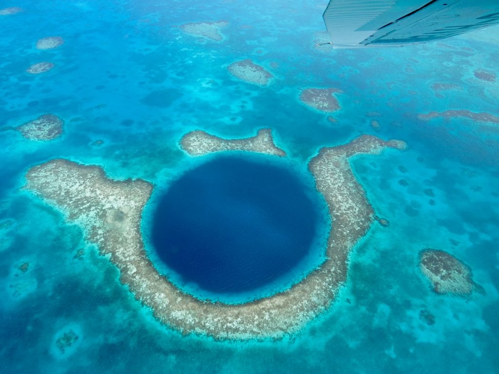 aerial view of belize great blue hole with a plane wing visible in one corner of the photo