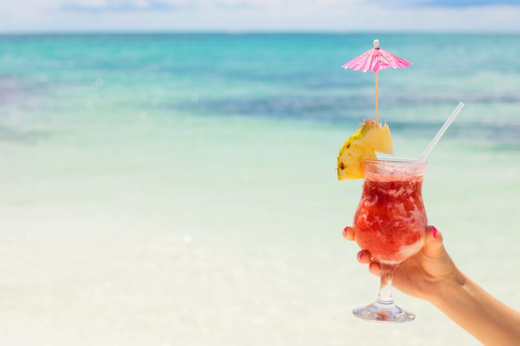 colorful tropical drink being held in front of bright blue water