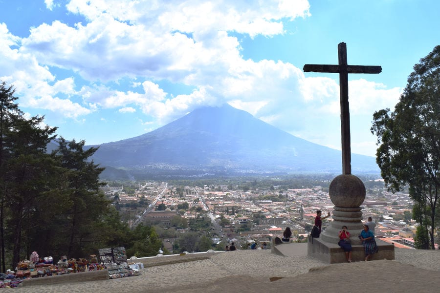 view of antigua from above with crucifix in the foreground and volcano in the background. this view is free to experience on a guatemala travel budget