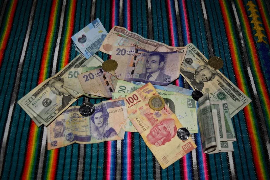 pile of money from various currencies sitting on a striped table cloth