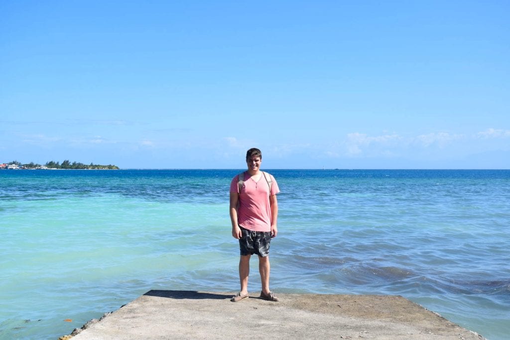 jeremy storm standing at the end of a dock overlooking the water in utila honduras wearing shorts and a t shirt, typical clothes for a packing list for central america mexico