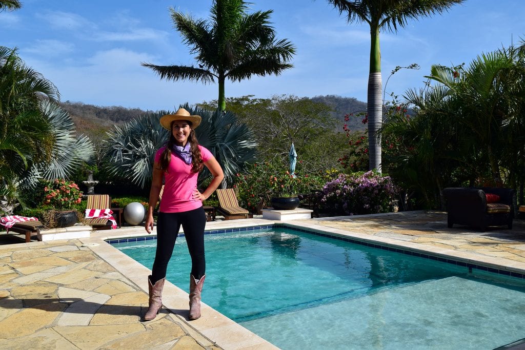kate storm in a pink shirt dressed up for riding, standing in front of a pool