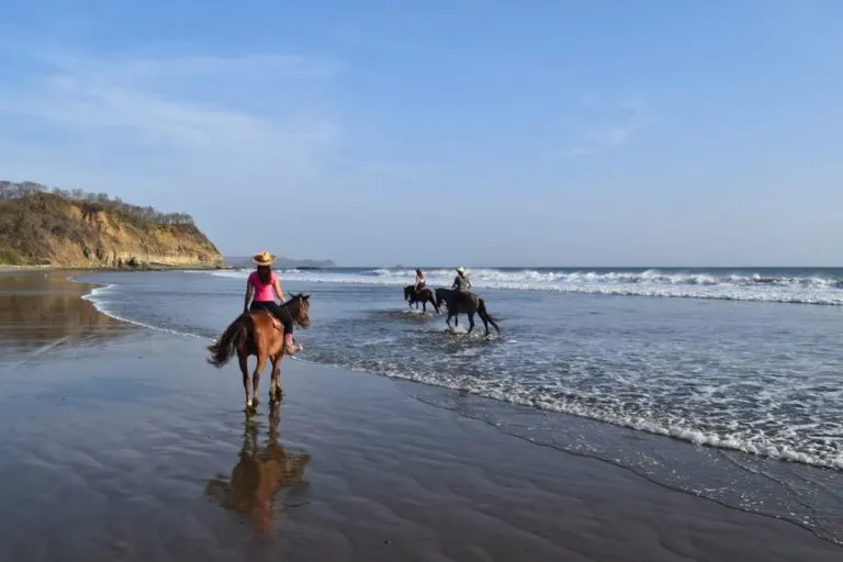 kate storm in a pink shirt horseback riding in nicaragua on a beach