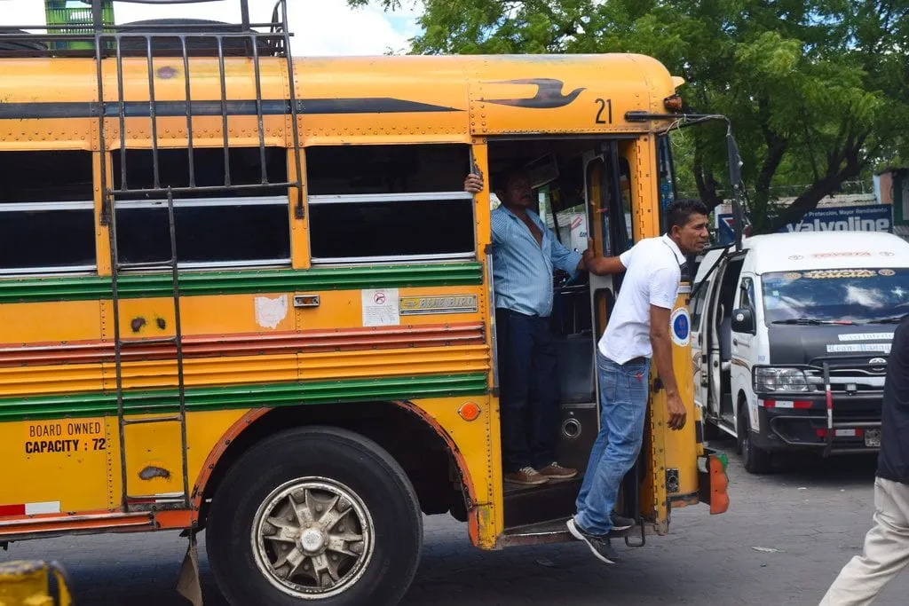 man hanging out of the front door of a chicken bus in nicaragua speaking to passerby