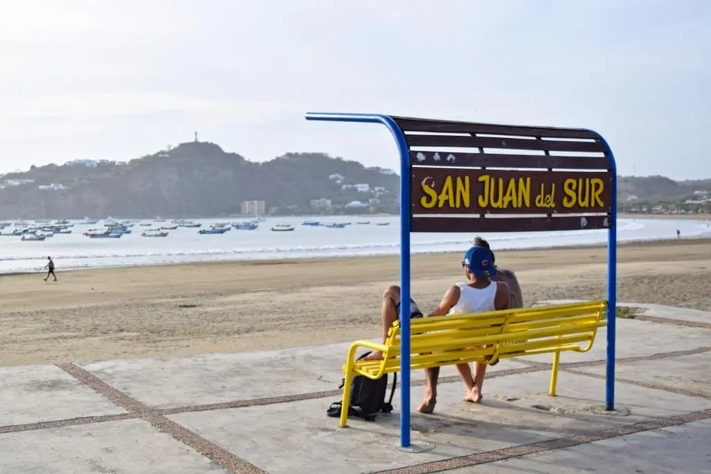 couple sitting on a yellow and blue bench in front of the san juan del sur nicaragua bench