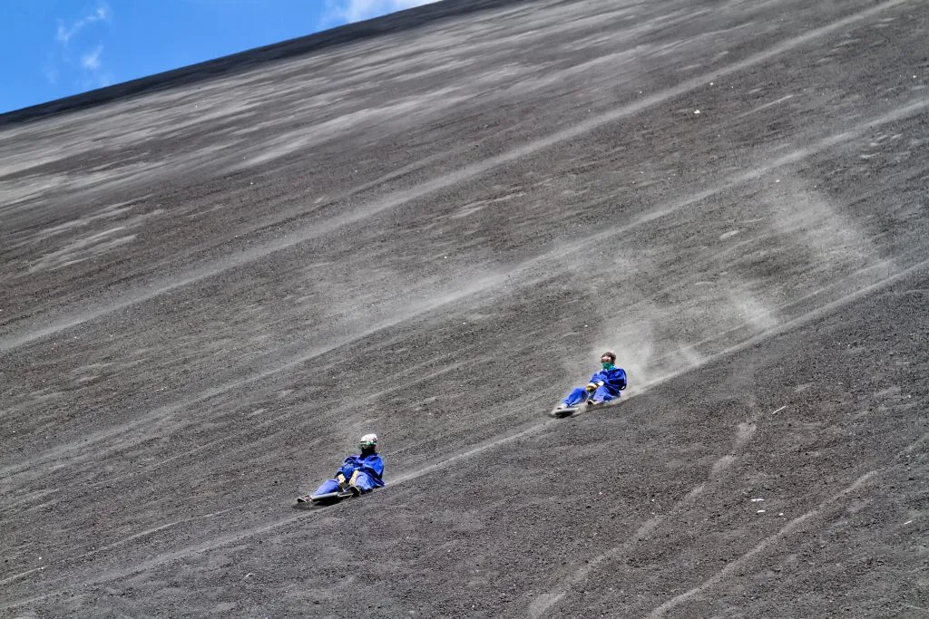 two volcano boarders in blue jumpsuits on volcano cerro negro