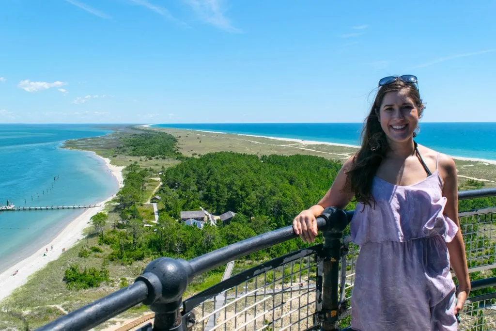 Kate Storm in a purple dress standing at the top of Cape Lookout lighthouse with the barrier island visible behind her