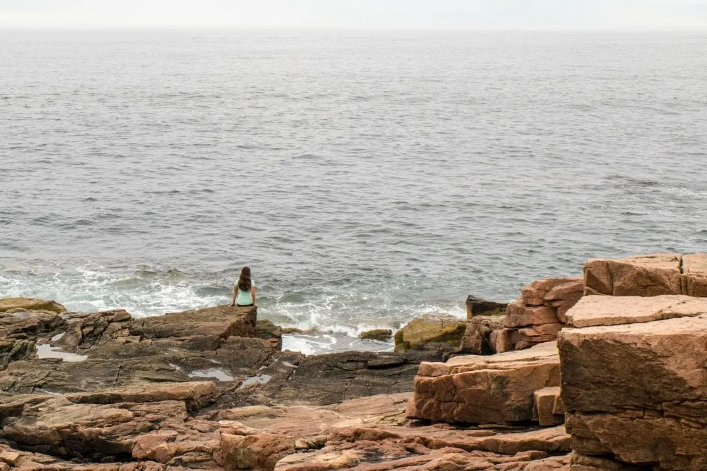 kate storm sitting on a rocky ledge near the atlantic ocean in maine