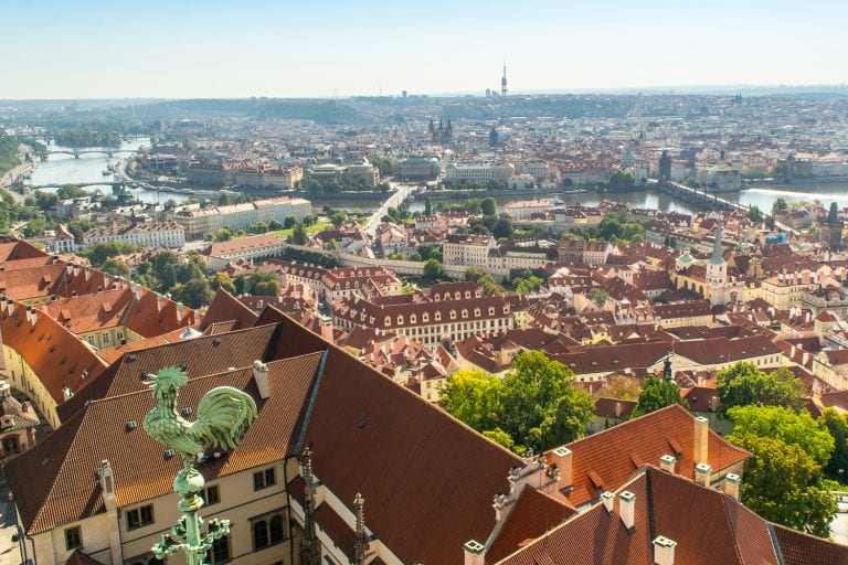 view of the prague skyline from the top of st vitus cathedral with a small green rooster in the left foreground