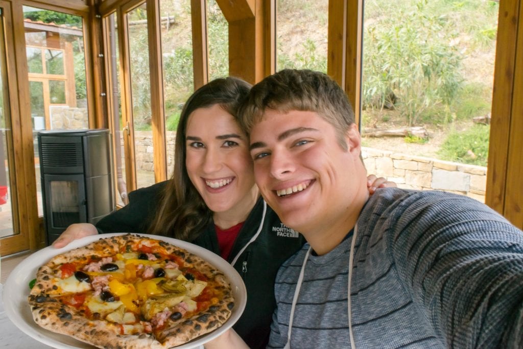 kate storm and jeremy storm holding up a pizza at a tuscany cooking class outside of florence italy