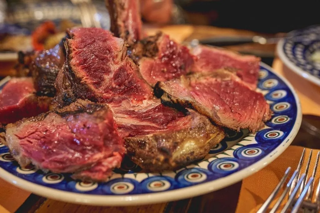 Sliced bistecca alla fiorentina on a blue and white plate, a must-try food in Florence Italy