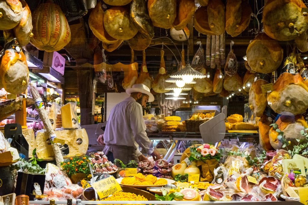 man cutting charcuterie surrounded by a display of meat in bologna italy