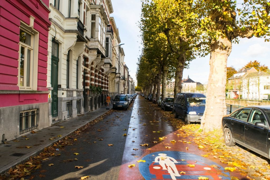 Empty street in Ghent Belgium with a few cars visible in the distance and yellow leaves on the ground--keep this damp weather in mind when making a fall packing list for Europe!