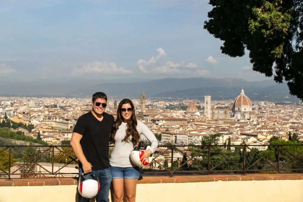 kate storm and jeremy storm holding helmets from a vespa tour in front of florence skyline view